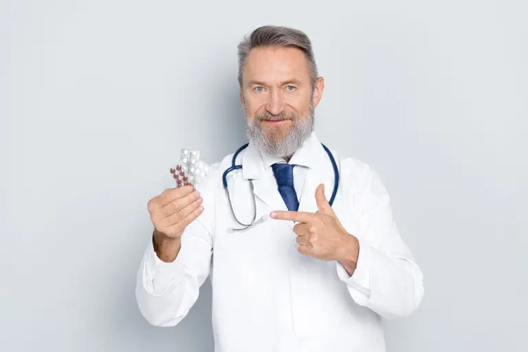 Ace Medicare Supplement: Everything You Need to Know A senior male doctor with a beard, wearing a white coat and a stethoscope, smiling and pointing at a pack of pills. Concept related to Ace Medicare Supplement.